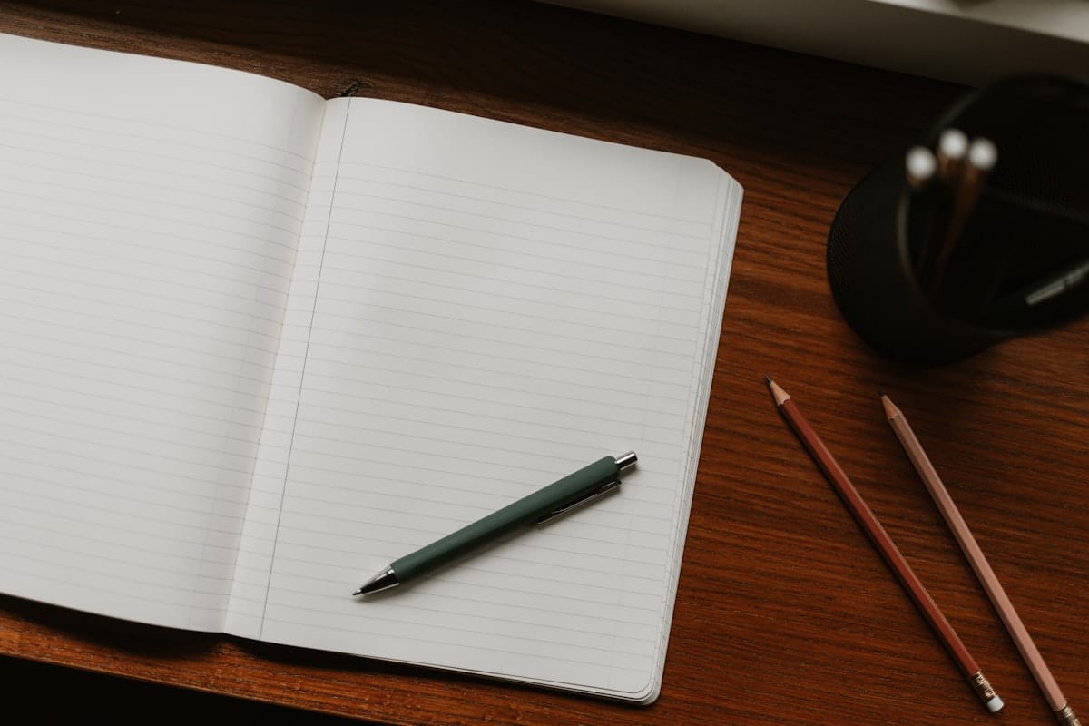 Open notebook with pen and pencils on a desk — a working tool, not a decorative one